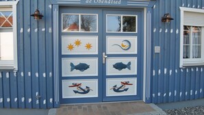 A building with a blue facade, a door with fish and star decorations, and the name 'de Obendtied' above it.