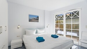 A hotel room with a bed, a nightstand, a desk, and a large window with a view of the outdoors.