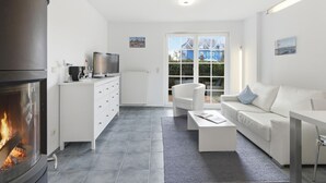 A modern living room with a fireplace, white furniture, and a view through large windows.