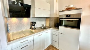 A compact kitchen with white cabinets, a built-in oven, a coffee maker, and a sink.