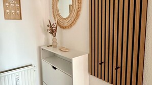 A room with a white radiator, a wall-mounted mirror, a wooden slat partition, and a small shelf with decorative items.