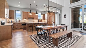 A modern kitchen with wooden cabinets, a central island, pendant lighting, and a dining area with a bench. - Red Ledges vista, hottub, golf, min 90 day stay (Heber City)