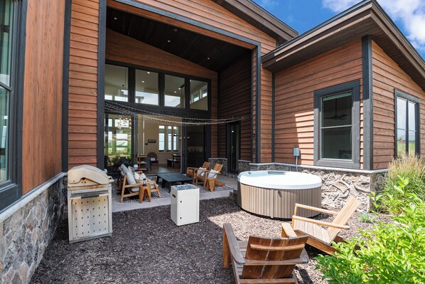 A modern house with a patio area featuring outdoor seating, a hot tub, and a stone wall.