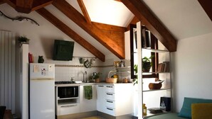 Une cuisine compacte avec des meubles blancs, une cuisinière et un four à micro-ondes. On y trouve un petit coin repas avec un canapé vert et un coussin jaune.