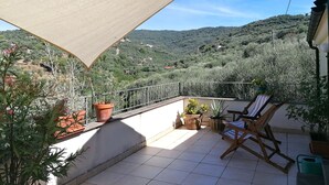 Un balcon donnant sur un paysage vallonné, avec des plantes en pot et une chaise en bois.