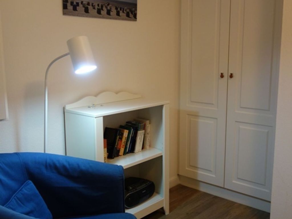 Une pièce avec une armoire blanche, une étagère blanche remplie de livres, un canapé bleu et un lampadaire blanc.