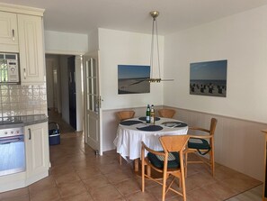A kitchen with white cabinets, a built-in oven, and a dining area with a round table and chairs. There are two framed pictures on the wall.