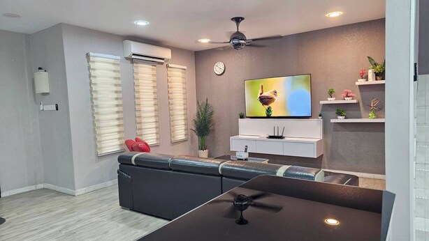 Een moderne woonkamer met een bank, een eettafel, inbouwspots, een plafondventilator, een televisie en een klok aan de muur.