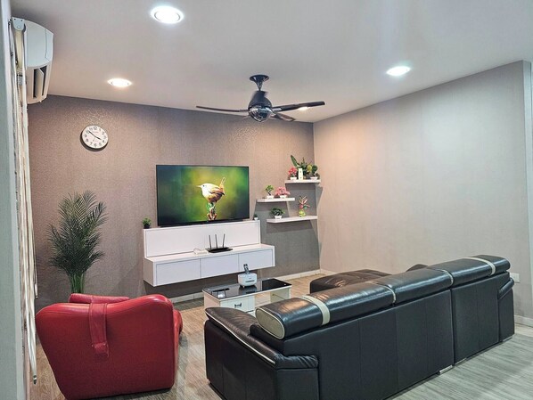 A modern living room with a flat-screen TV, a ceiling fan, a sofa, a red chair, and a small plant.