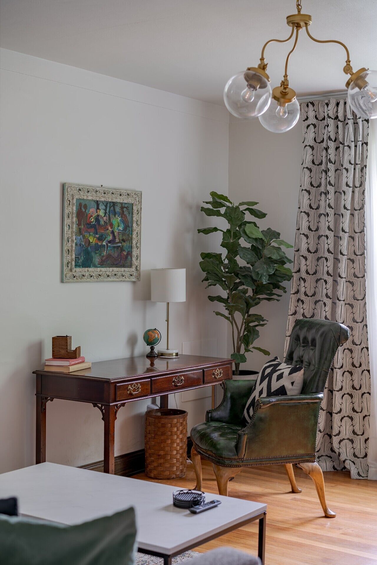 Een kamer met een bureau, stoel, lamp, wereldbol en een grote plant.