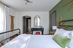 Een hotelkamer met een bed, bureau, spiegel, stoel en een raam met gordijnen.