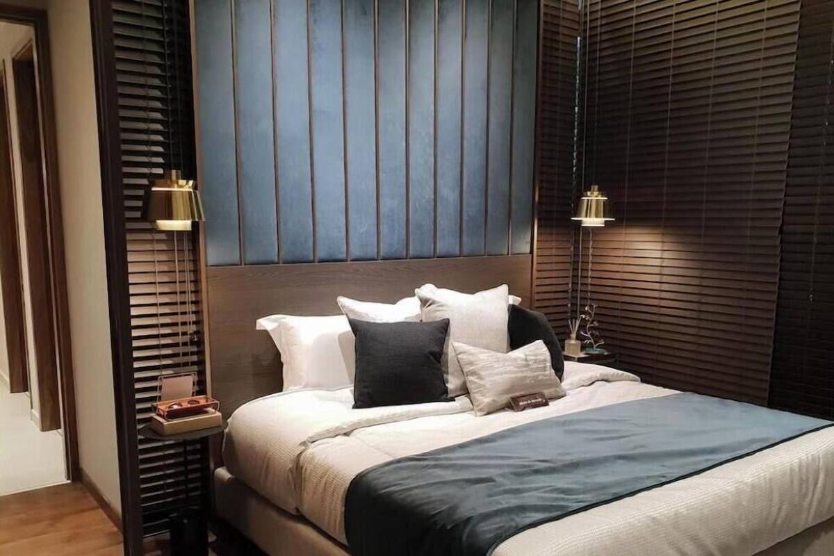 A modern bedroom with a large bed, wooden headboard, bedside tables, and a nightstand with a lamp.
