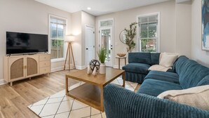 A modern living room with a large flat-screen TV, a wooden coffee table, a blue sofa, and a white rug. - Spacious 3-Bedroom Home with King Suite, Parking Permits, and Prime Location Near Downtown Columbus (Columbus)