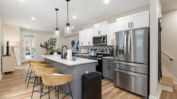 A modern kitchen with a central island, stainless steel appliances, and a dining area with wicker chairs. - Spacious 3-Bedroom Home with King Suite, Parking Permits, and Prime Location Near Downtown Columbus (Columbus)