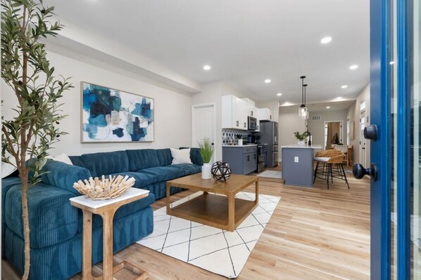 Un soggiorno moderno con un divano blu, un tavolino in legno e una cucina sullo sfondo.