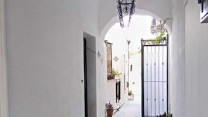 A narrow, white-walled corridor with a tiled floor, flanked by potted plants and a hanging light fixture. - Studio apartment with kitchen in Center "Stay in Catania" (Catania)