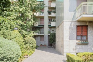 A courtyard with a stone pathway, surrounded by greenery and a multi-story building with balconies. - Easylife - Contemporary design on the Navigli (Milano)