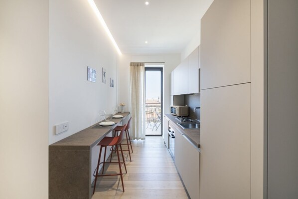 A modern kitchen with a long countertop, bar stools, and a view to an outdoor balcony. - Easylife - Contemporary design on the Navigli (Milano)