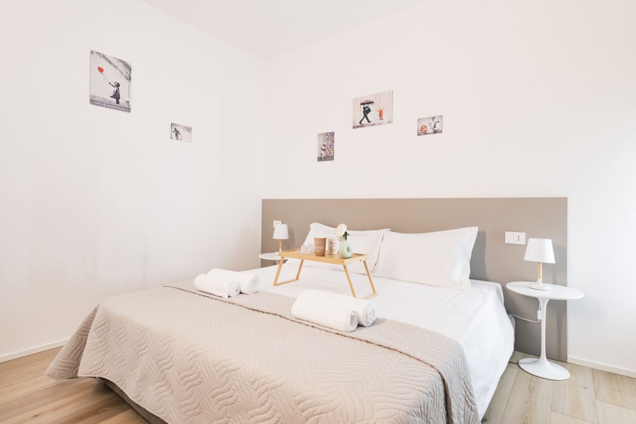 Habitación de hotel con una cama grande, una mesita de noche con lámpara, una pequeña mesita auxiliar y obras de arte en las paredes.