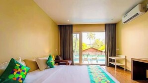 A hotel room with a bed, a desk, and a view of a pool and palm trees. - Skazka Beach Resort (Mandrem)