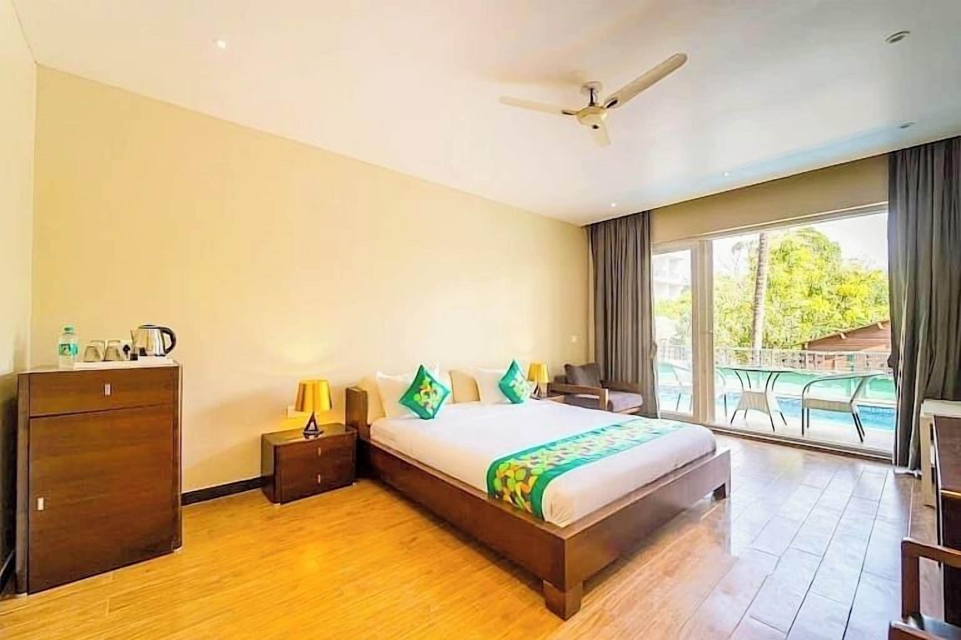 Ein Hotelzimmer mit einem großen Bett, einem Deckenventilator, einer Holzkommode und Blick auf einen Pool.