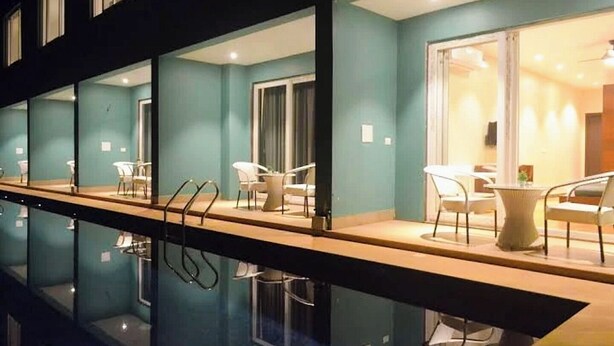 A hotel room with a pool, a dining area with chairs and tables, and a large window with curtains. - Skazka Beach Resort (Mandrem)