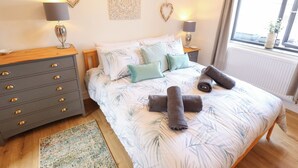 A bedroom with a bed, nightstands, a dresser, decorative wall art, and a window with a view. - Sandy Toes (Mablethorpe)