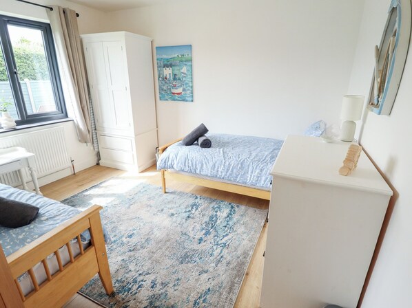 A bedroom with a single bed, a small desk, a wardrobe, and a painting on the wall.