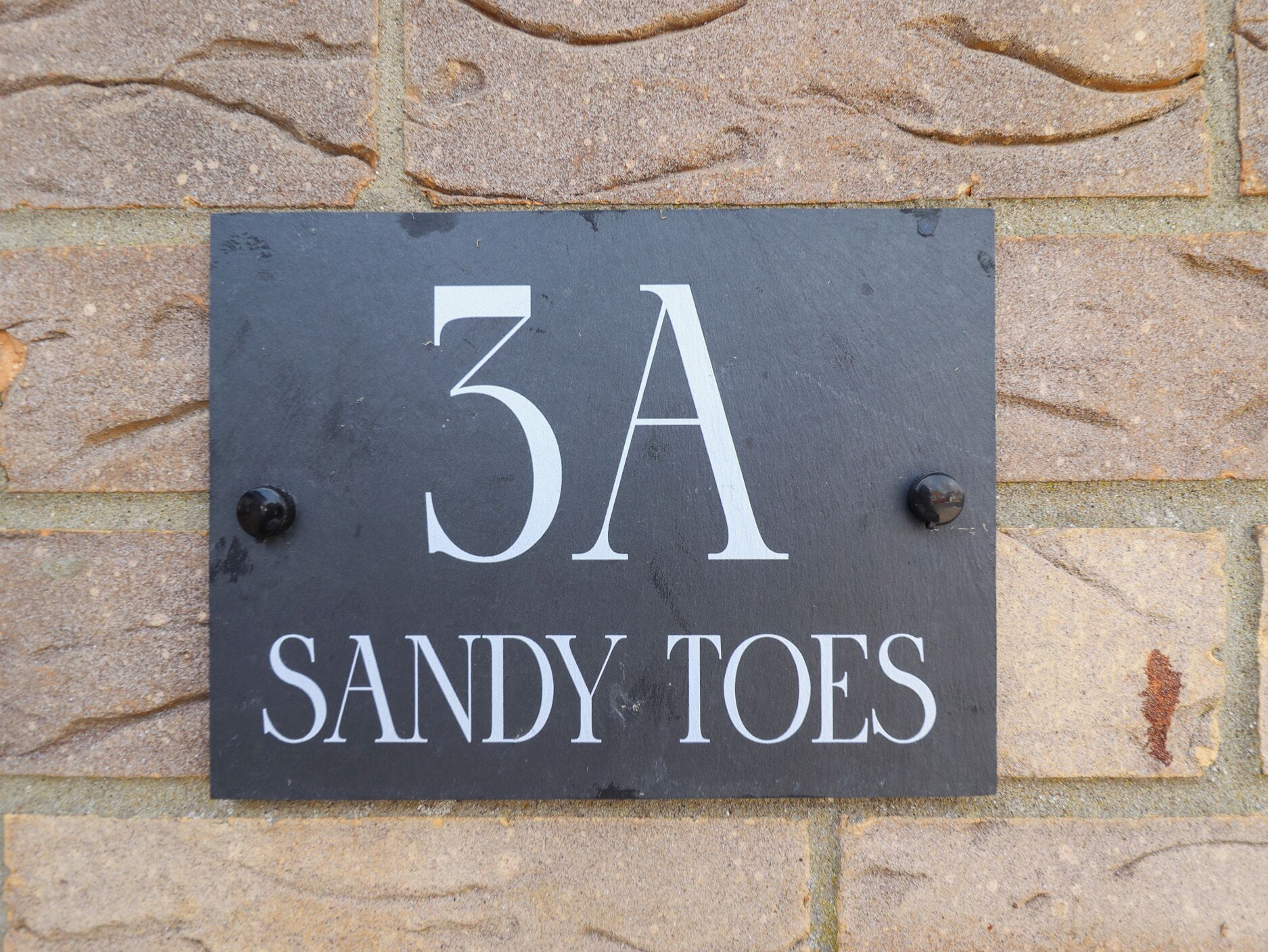 A house number sign with '3A' and 'SANDY TOES' written on it.