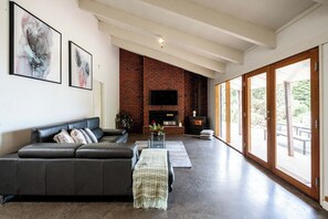 A modern living room with a brick fireplace, a leather sofa, and a flat-screen TV. - Seaside Country Escape (Torquay)