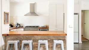 A modern kitchen with a central island, a gas stove, and a stainless steel range hood. There are three bar stools in front of the island. - Seaside Country Escape (Torquay)