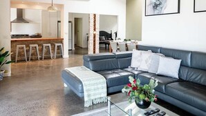 A spacious living area with a modern sofa, a glass coffee table, and a kitchen in the background. - Seaside Country Escape (Torquay)