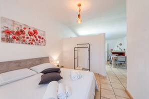 A bedroom with a bed, pillows, a towel rack, a desk, and a chair.
