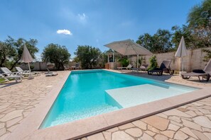 A rectangular swimming pool with a stone border, surrounded by lounge chairs and umbrellas.