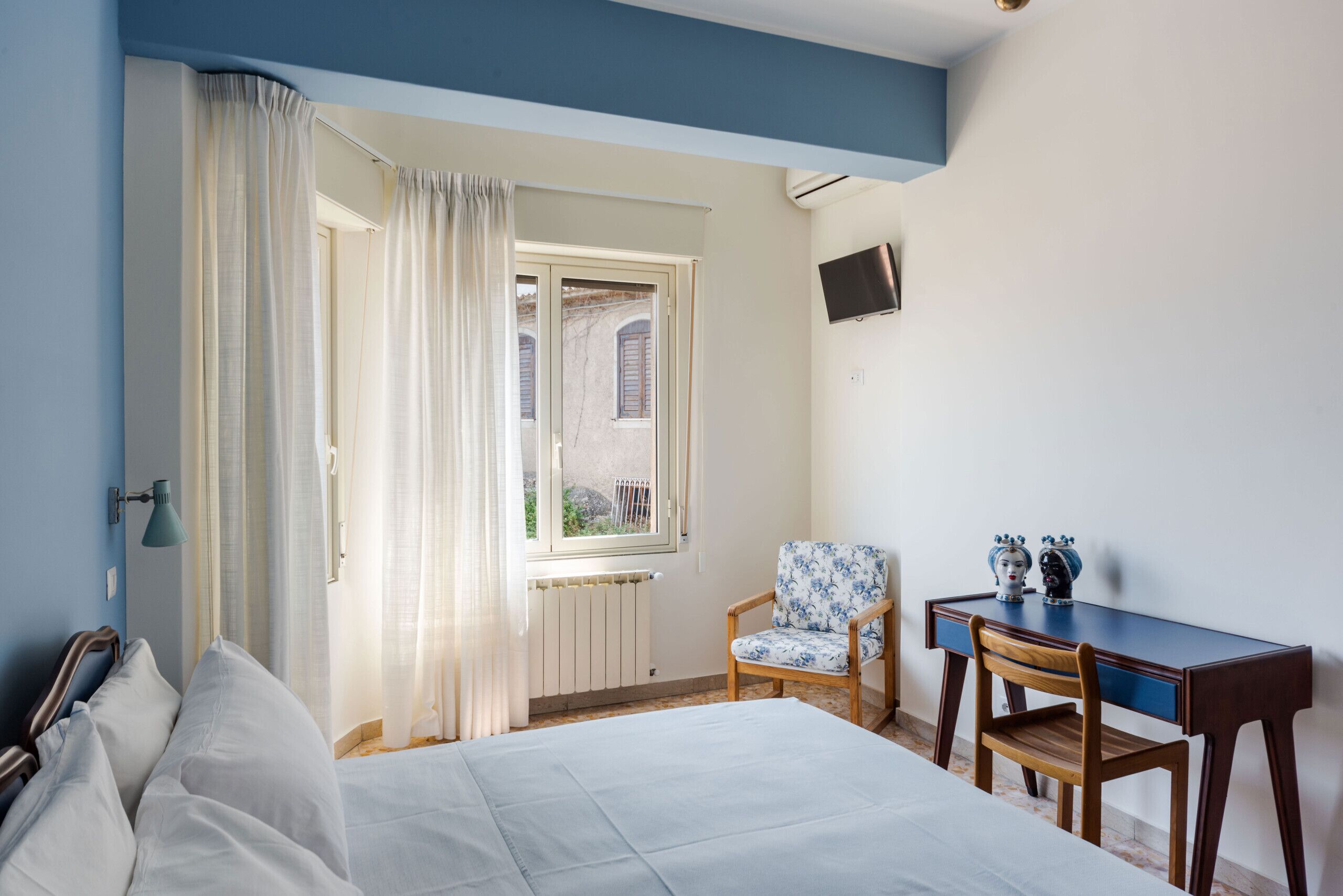 Un dormitorio con cama, una silla, un escritorio y una ventana con cortinas.