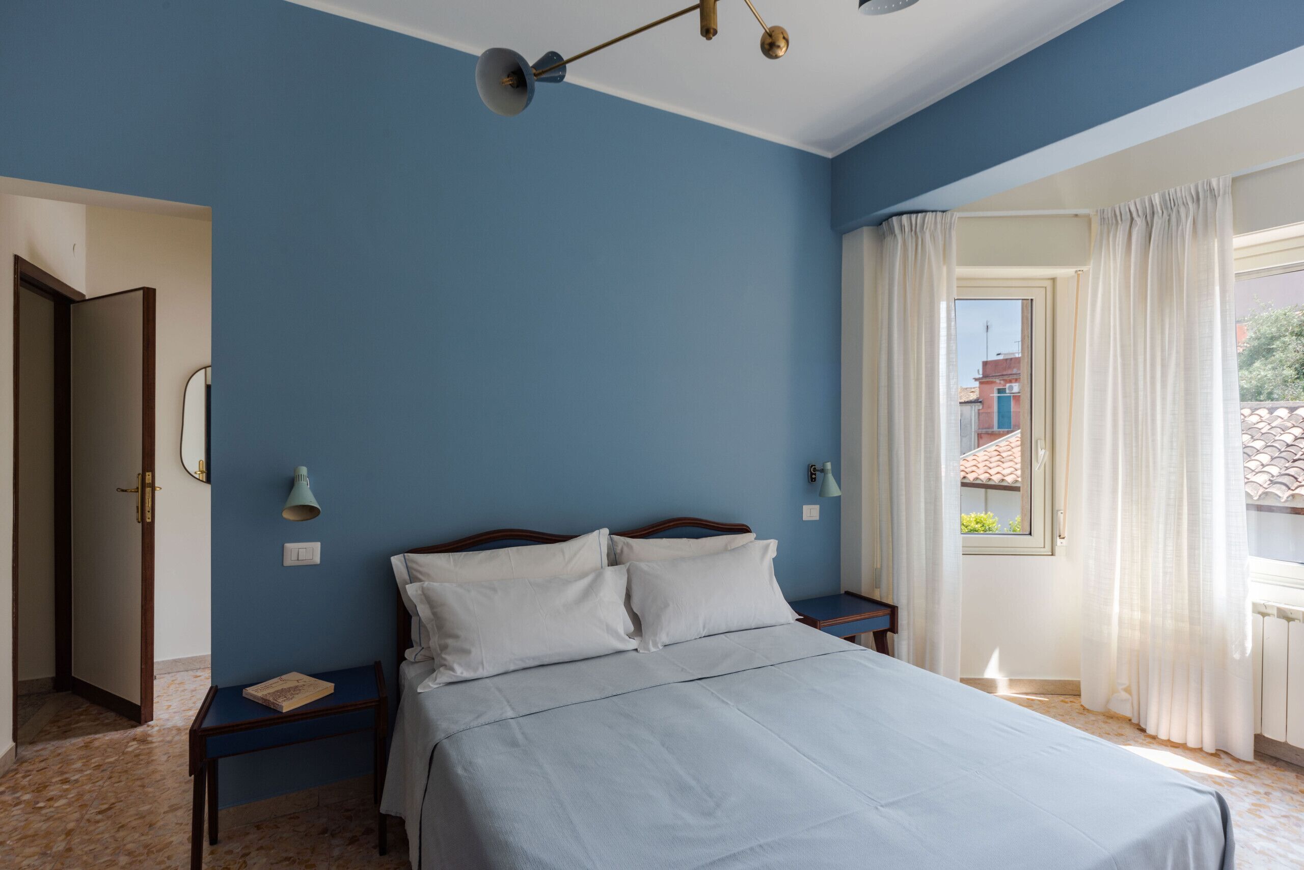 A bedroom with a bed, two bedside tables, a nightstand, a window with curtains, and a door.