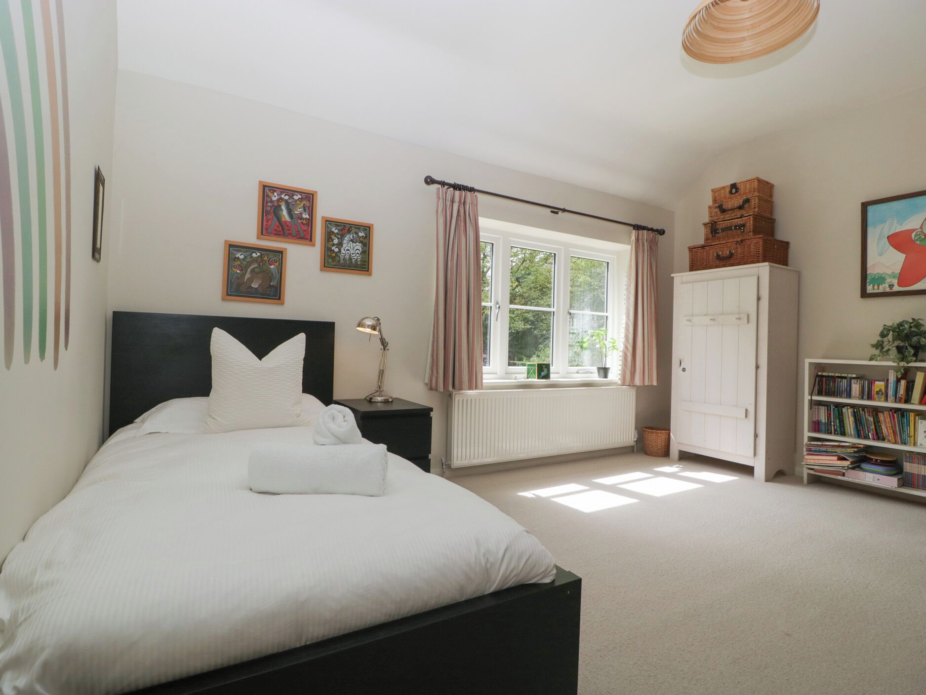 A neatly arranged bedroom with a bed, bedside lamp, window with curtains, radiator, and a bookshelf.