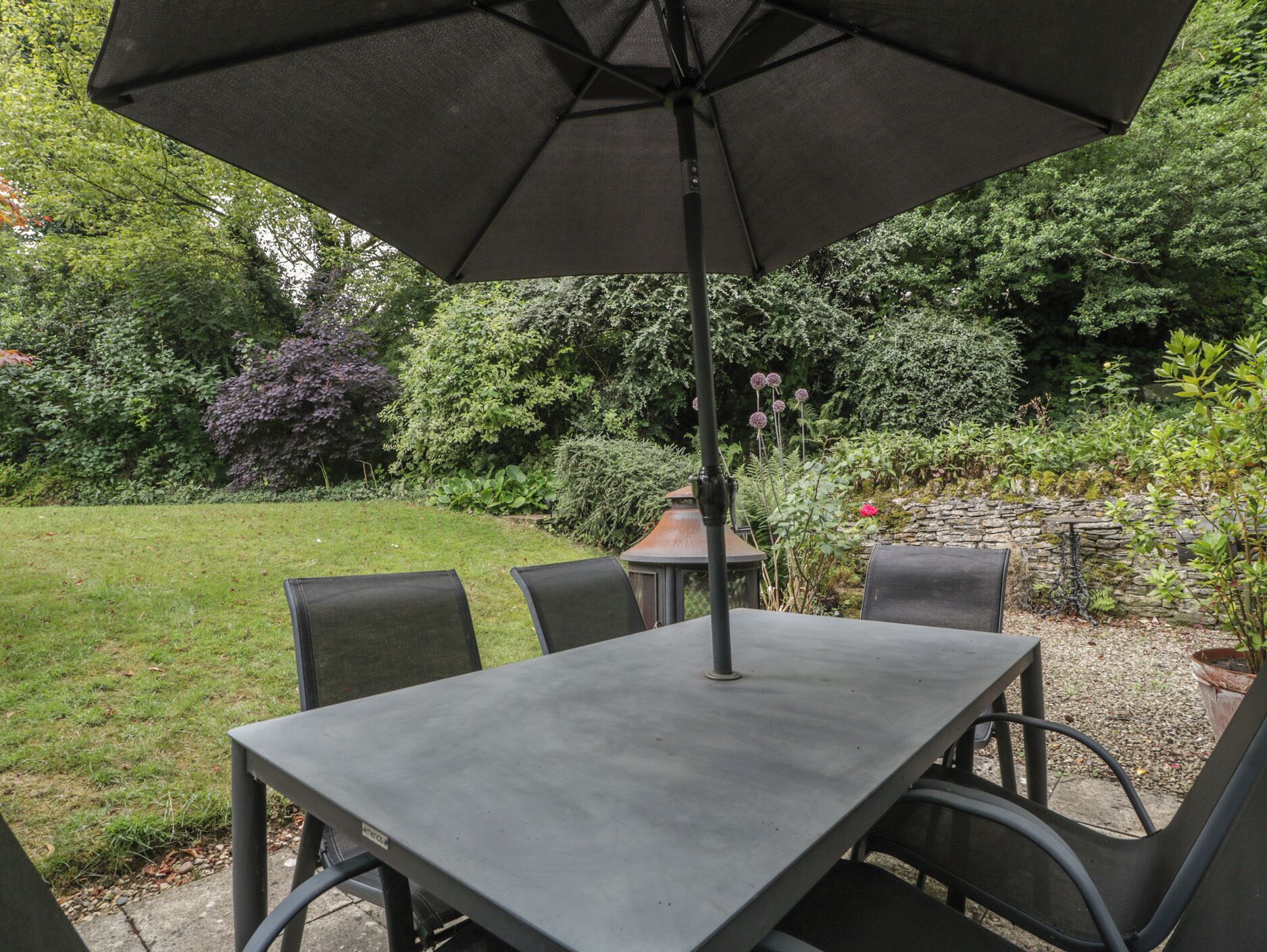A patio with a table and chairs, surrounded by greenery and a stone wall.