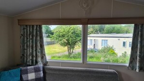 Ein Zimmer mit großem Fenster, einem Sofa mit gemusterten Kissen und Blick auf ein Haus und Grünfläche.