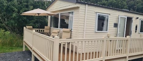 A mobile home with a deck, outdoor seating, and a covered patio area.
