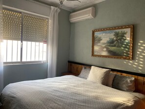 A bedroom with a bed, a painting, an air conditioner, and a window with blinds. - Santa Ana En La Playa Lo Pagan (San Pedro del Pinatar)