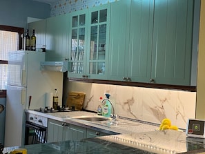 Une cuisine avec des meubles de couleur vert clair, un plan de travail en marbre, un évier en acier inoxydable et une cuisinière.