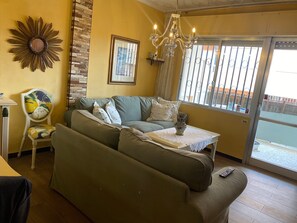 A living room with a sofa, a chair, a table with a vase, a chandelier, a framed picture, and a window with bars. - Santa Ana En La Playa Lo Pagan (San Pedro del Pinatar)
