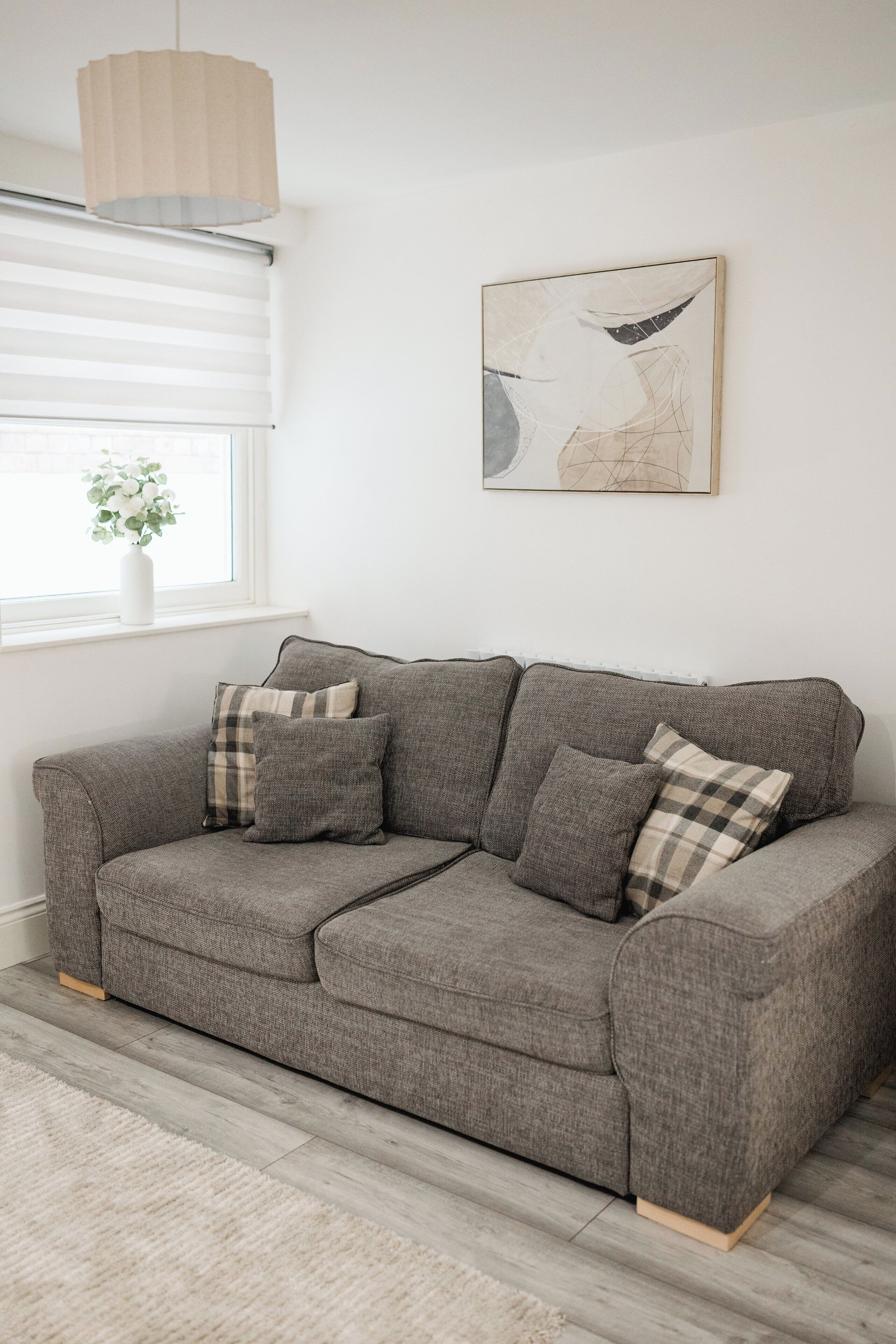 A grey sofa with checkered cushions, a white vase with flowers, and a painting on the wall.