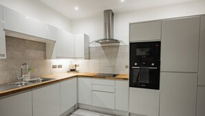 Eine moderne Küche mit weißen Schränken, einer Edelstahl-Dunstabzugshaube, einem Bosch-Backofen und einem Spülbecken mit Armatur.