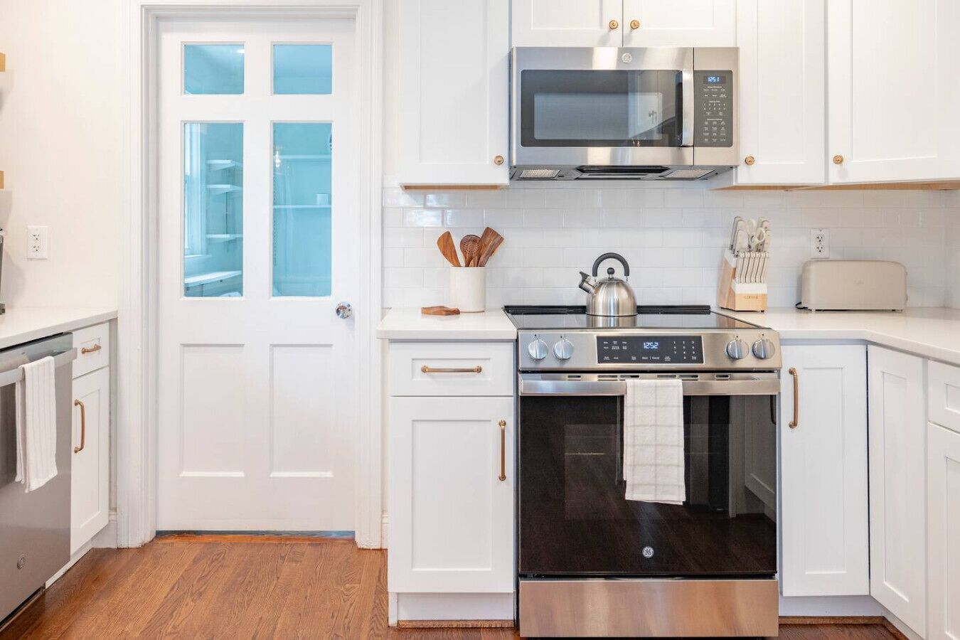 Una cocina moderna con muebles blancos, un horno de acero inoxidable, un microondas y un tostador.