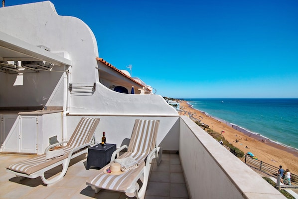 A balcony with two sun loungers, a small table with a bottle, and a view of the beach.