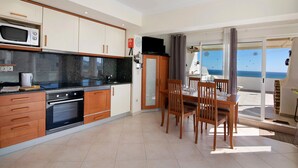 A modern kitchen with a microwave, oven, and dining area with chairs and a table. - Apartment 'Vista Mar' with Sea View, Wi-Fi and Air Conditioning (Albufeira)