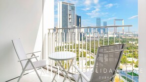 A balcony with a white chair, a small round table, and a city view of Dubai's skyline. - LUX The Downtown Zabeel View Suite (Dubai)