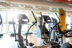 Un gimnasio con diferentes máquinas de ejercicio, un interior luminoso y un amplio ventanal.